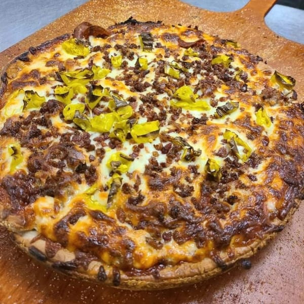 A Castaways bar-and-grill pizza, topped with ground meat and green peppers, on a wooden pizza peel.