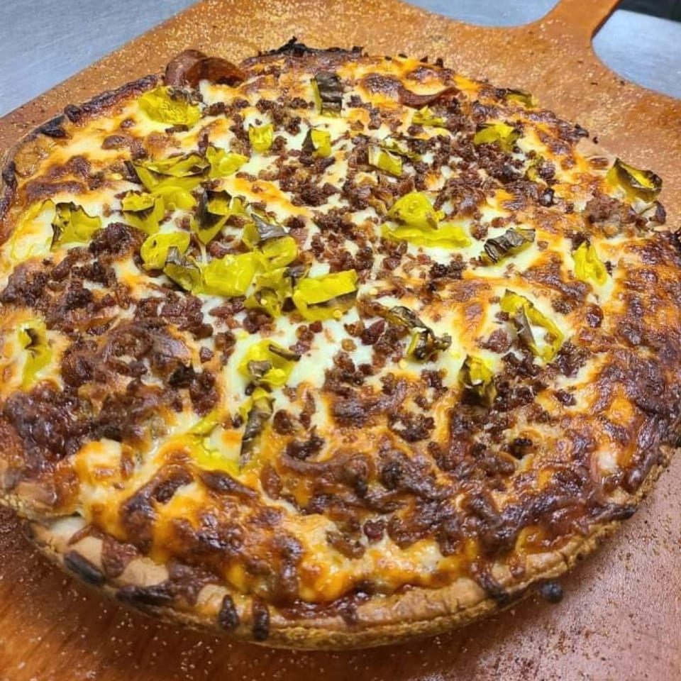 A Castaways bar-and-grill pizza, topped with ground meat and green peppers, on a wooden pizza peel.