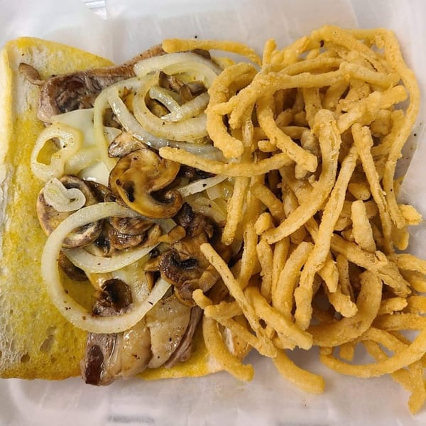 A Castaways steak sandwich with mushrooms, onions, and cheese, served with crispy onion rings.