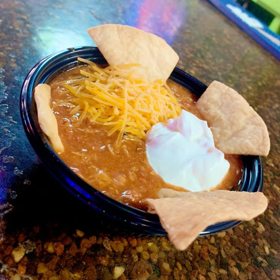 Castaways' chili with shredded cheese, sour cream, and tortilla chips in a dark bowl.