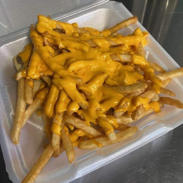 A white takeout container filled with golden french fries generously topped with melted yellow cheese.