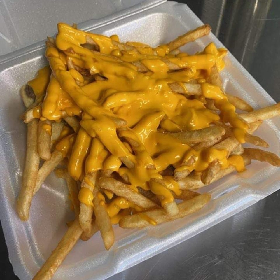 A white takeout container filled with golden french fries generously topped with melted yellow cheese.